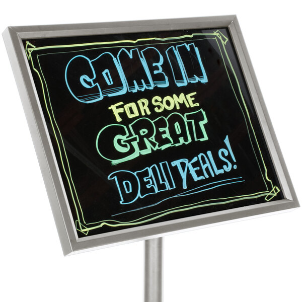 A black Aarco marker board with chrome frame on a deli counter with writing that says "Come for some great deliveries" in neon.