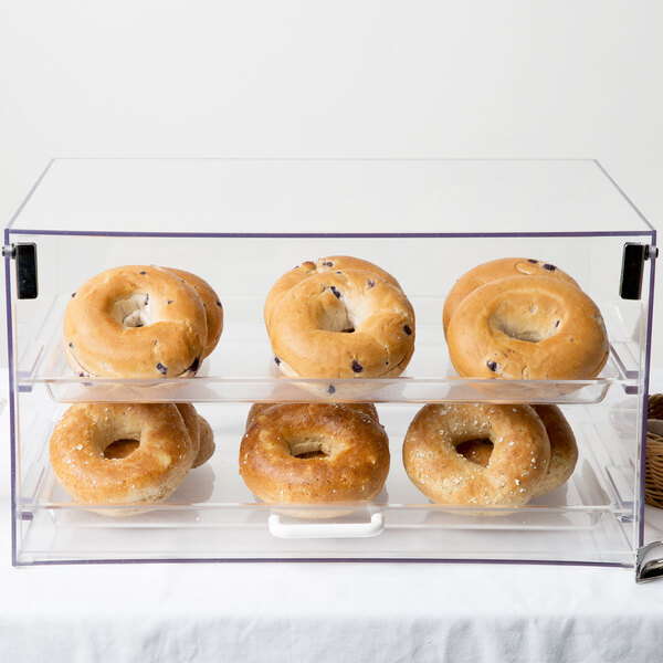 A Cal-Mil two-tier acrylic display case filled with bagels and donuts.