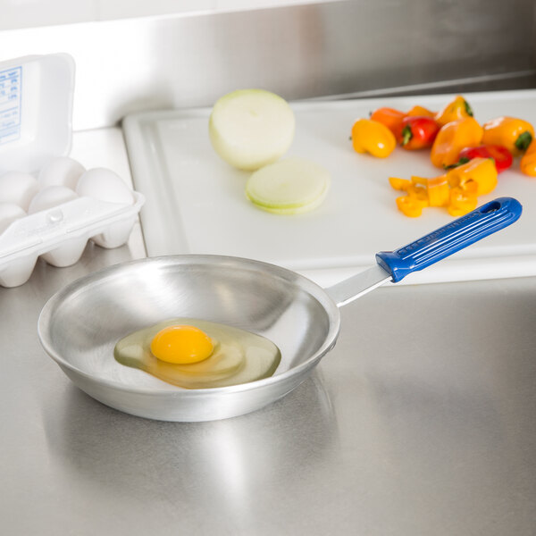A Vollrath Wear-Ever aluminum fry pan with egg yolk and vegetables on a counter.