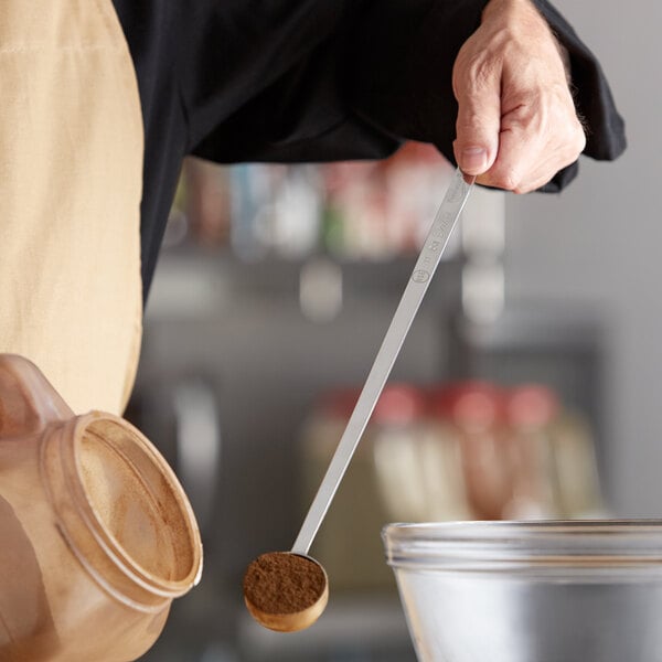 A person using a Vollrath long handled measuring spoon to stir brown powder in a bowl.