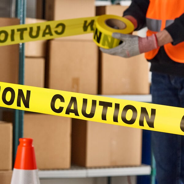 A roll of yellow caution tape being used in a warehouse setting.