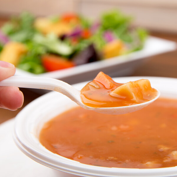 A Dart white plastic soup spoon being held over a bowl of soup.