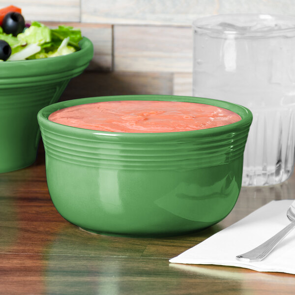 A green Fiesta china bowl with salad in it on a table.