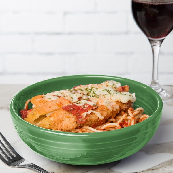 A green Fiesta china bowl filled with food next to a glass of wine.