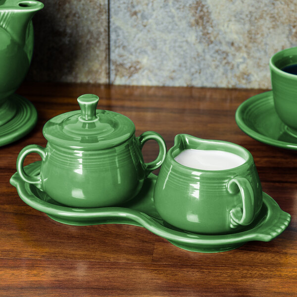 A green Fiesta sugar and creamer tray on a wooden surface.