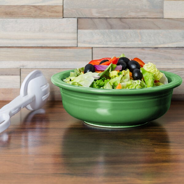 A green Fiesta serving bowl filled with salad on a wooden surface.