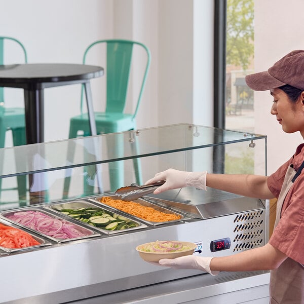 A glass sneeze guard installed on a refrigerated prep table in a restaurant setting.