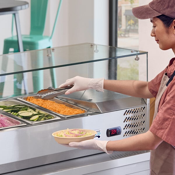 A glass sneeze guard installed on a refrigerated prep table at a food service counter.
