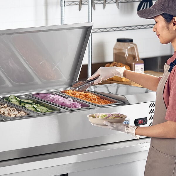 A stainless steel Avantco CPT-60 59-inch countertop refrigerated prep rail filled with various fresh vegetables and being used by a food service worker.