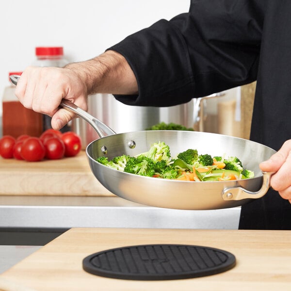 A person using a Vollrath Miramar 10" Saute Pan to cook broccoli and carrots.