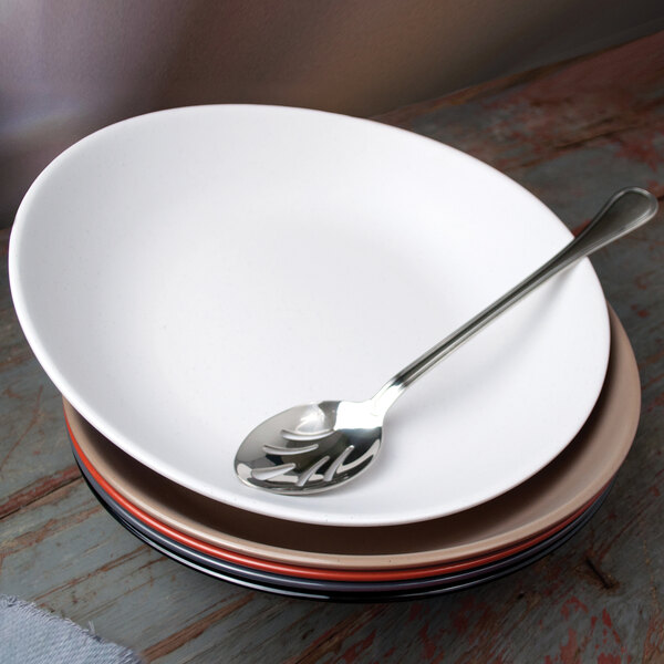 A white Libbey melamine serving bowl on a white surface with a spoon in it.