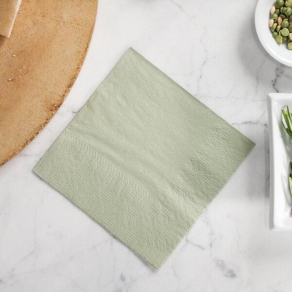 A soft sage green Hoffmaster beverage napkin on a table with a bowl of beans and peanuts.