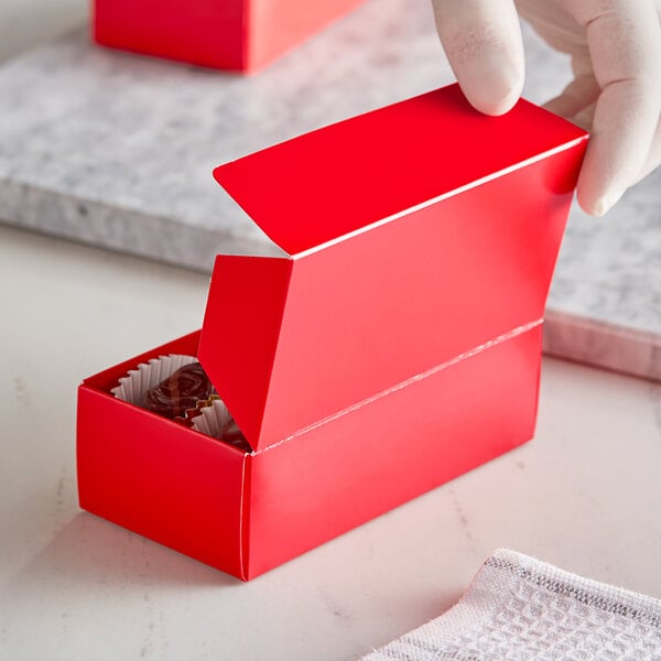 A person's hand holding a red 1/2 lb. candy box with white border and candy inside.