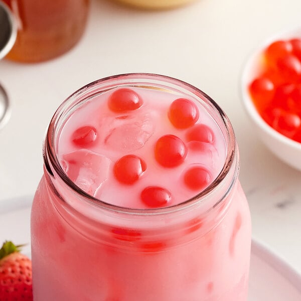 A glass jar filled with pink liquid and red berries.