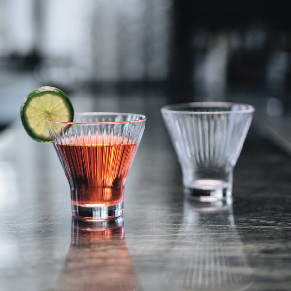 Two Arcoroc stemless cocktail glasses filled with drinks and garnished with lime wedges on a bar counter.