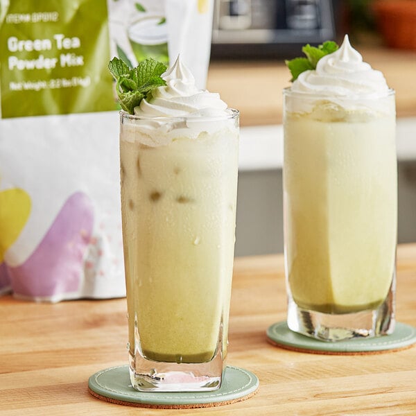 A close-up of a glass of green liquid with whipped cream and mint leaves on top.