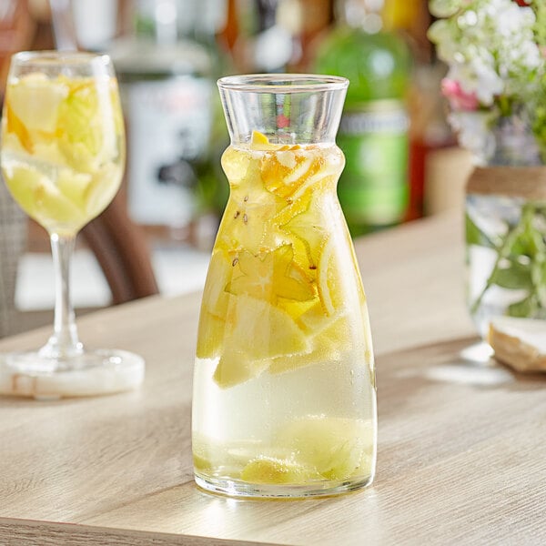 An Arcoroc glass carafe filled with a drink and fruit on a table.