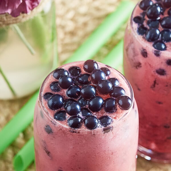 A glass of pink smoothie with blueberry bursting boba.