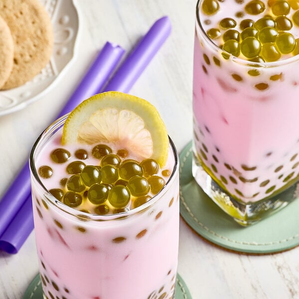 A glass of bubble tea with pink liquid and green bubbles.