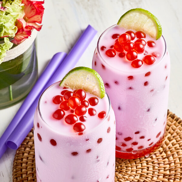 A glass of pink milkshake with Bossen cherry boba and a lime wedge.