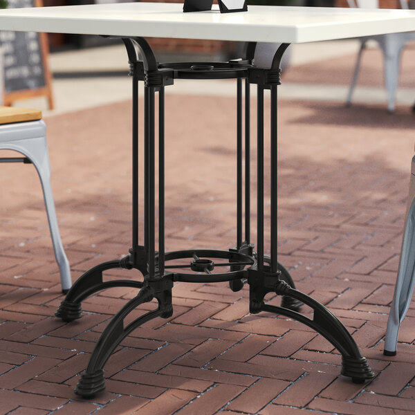 A black cast iron Art Marble Furniture table base on a brick surface with two chairs.