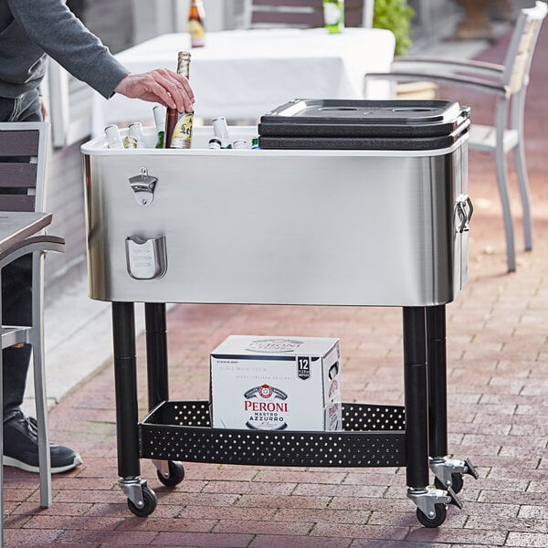 A man standing next to a stainless steel Choice beverage cooler cart with bottles in it.