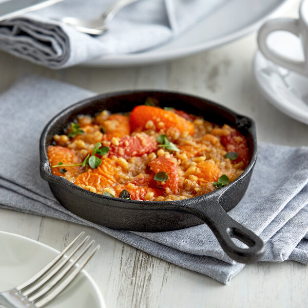 A Vollrath pre-seasoned mini cast iron skillet filled with food on a table in a farm-to-table restaurant.