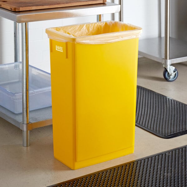 A yellow Lavex rectangular trash can with a white plastic bag sits on a kitchen floor.