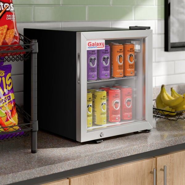 A small black countertop refrigerated merchandiser with a glass door, displaying assorted canned beverages inside.