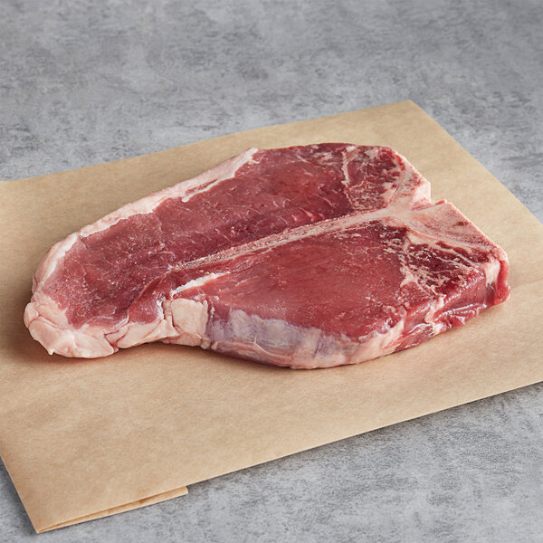 A piece of raw Warrington Farm Meats Porterhouse steak on a paper.
