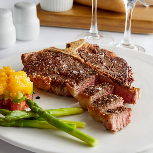 A plate with a Warrington Farm Meats Porterhouse steak and asparagus with a glass of wine on the side.