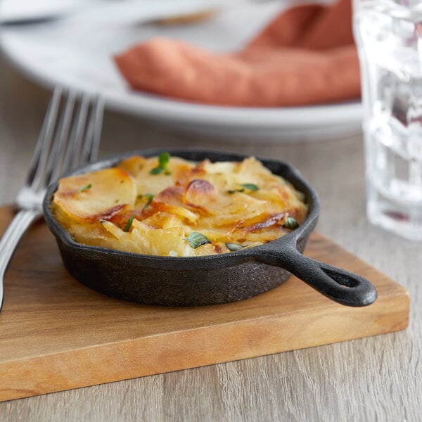 A small Vollrath cast iron skillet filled with food on a wooden board.