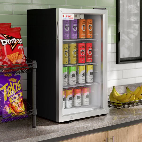 A black Galaxy CRG-4 customizable countertop display refrigerated merchandiser with a glass door, stocked with assorted canned beverages.