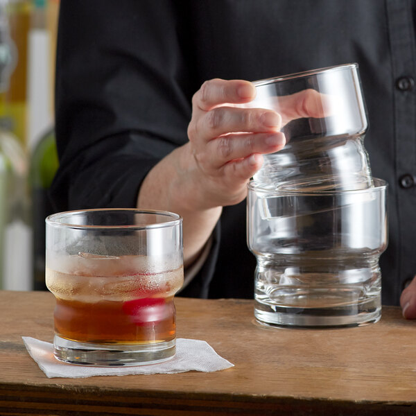 A person pouring a drink into two Libbey Stackable Rocks glasses filled with ice on a table in a cocktail bar.