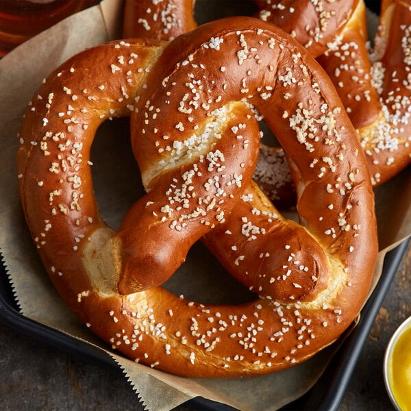 Two soft pretzels with white salt on top in a basket with mustard