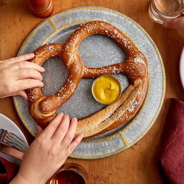 Hands grabbing traditional twist soft pretzel on plate with mustard