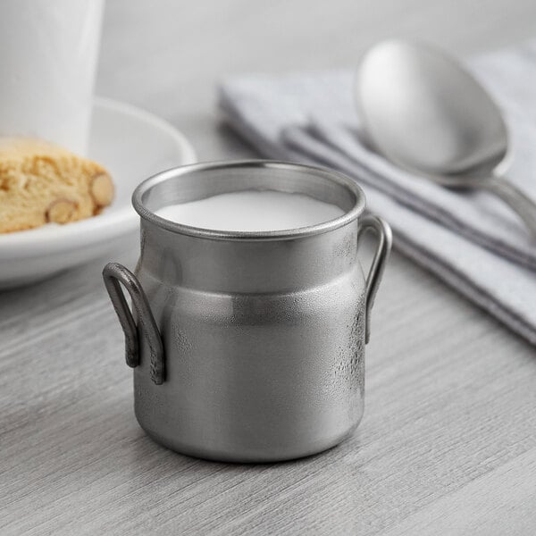 A stainless steel Vollrath mini milk can with milk in it.