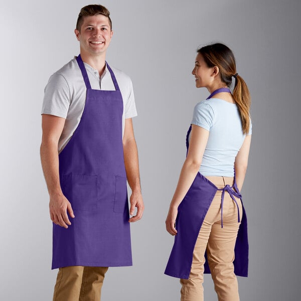 A man and woman standing in front of each other wearing bright purple aprons.