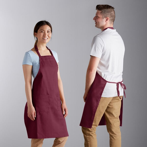 A man and woman wearing burgundy aprons in a professional kitchen.
