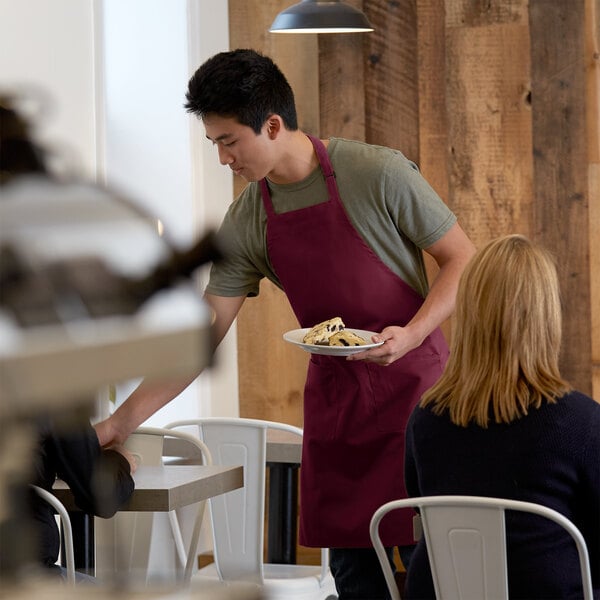 A man in a burgundy bib apron serving food.