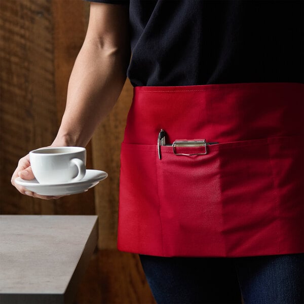 A person wearing a red Choice apron holding a cup and saucer.