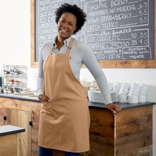 A woman wearing a Choice khaki bib apron standing in front of a counter.