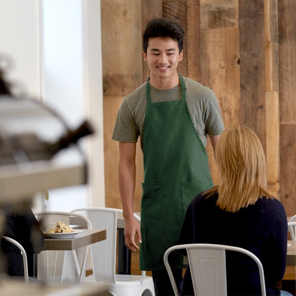 A man wearing a Choice Hunter Green apron standing next to a table.