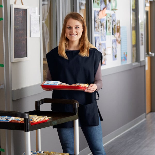 A woman wearing a navy blue cobbler apron holding a tray of food.