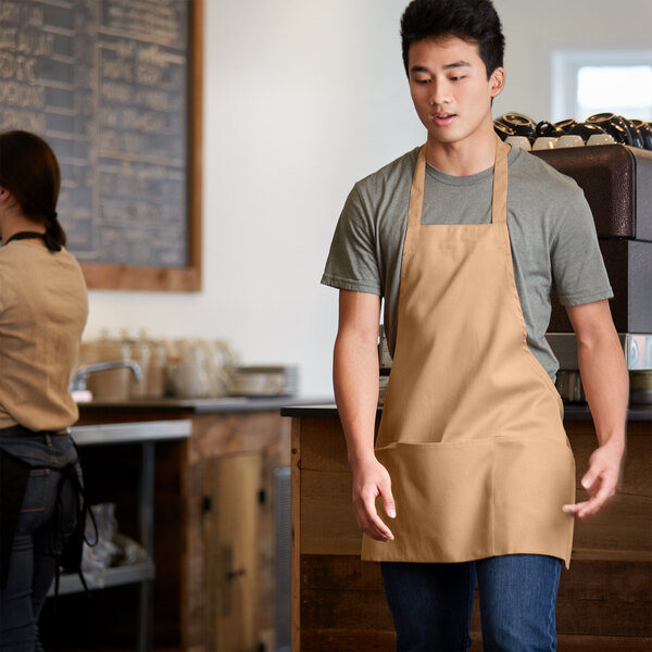 A man wearing a khaki Choice bib apron with 3 pockets.
