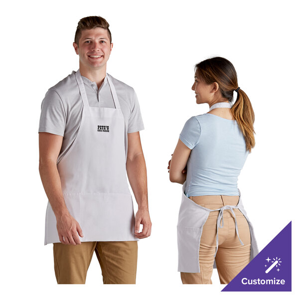 A man and woman wearing white customizable front of house bib aprons.