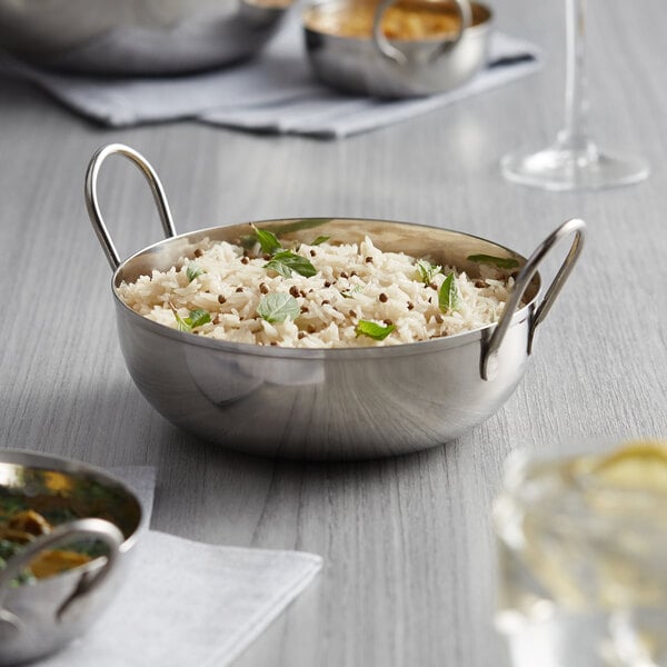 A Vollrath shallow stainless steel balti dish filled with rice on a table in an Asian restaurant.