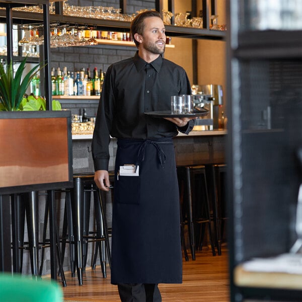 A man wearing a navy blue bistro apron holding a tray with glasses.