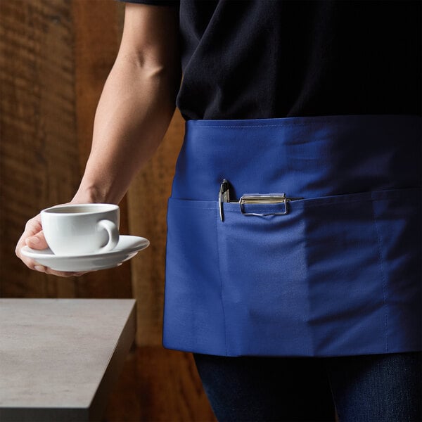 A person wearing a Choice royal blue apron holding a cup of coffee.