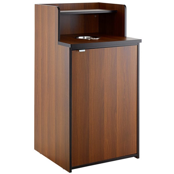 A wooden cabinet for a Lancaster Table & Seating Walnut Receptacle with a drop hole and a shelf.